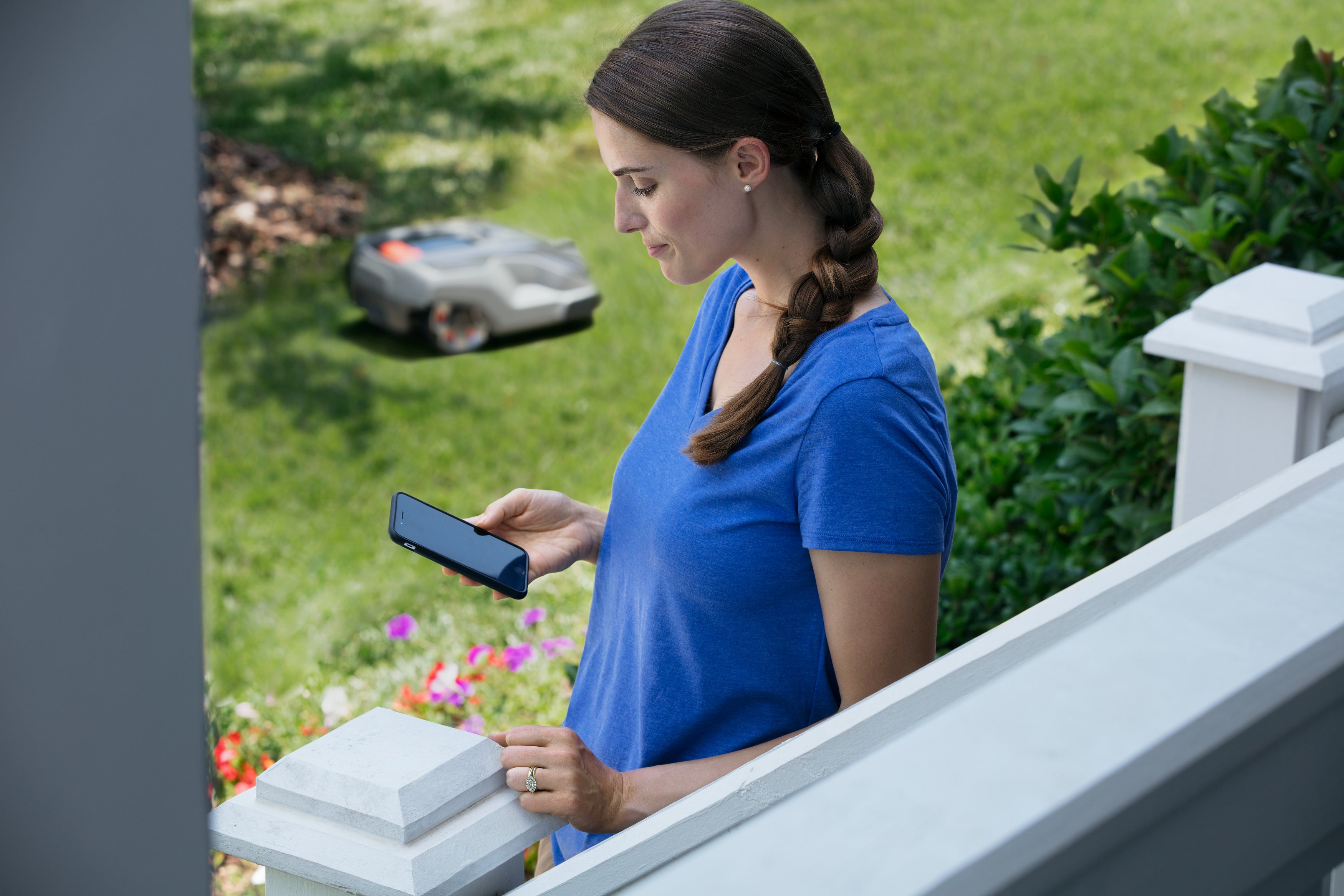 Жінка зі смартфоном і косарка Automower на подвір’ї